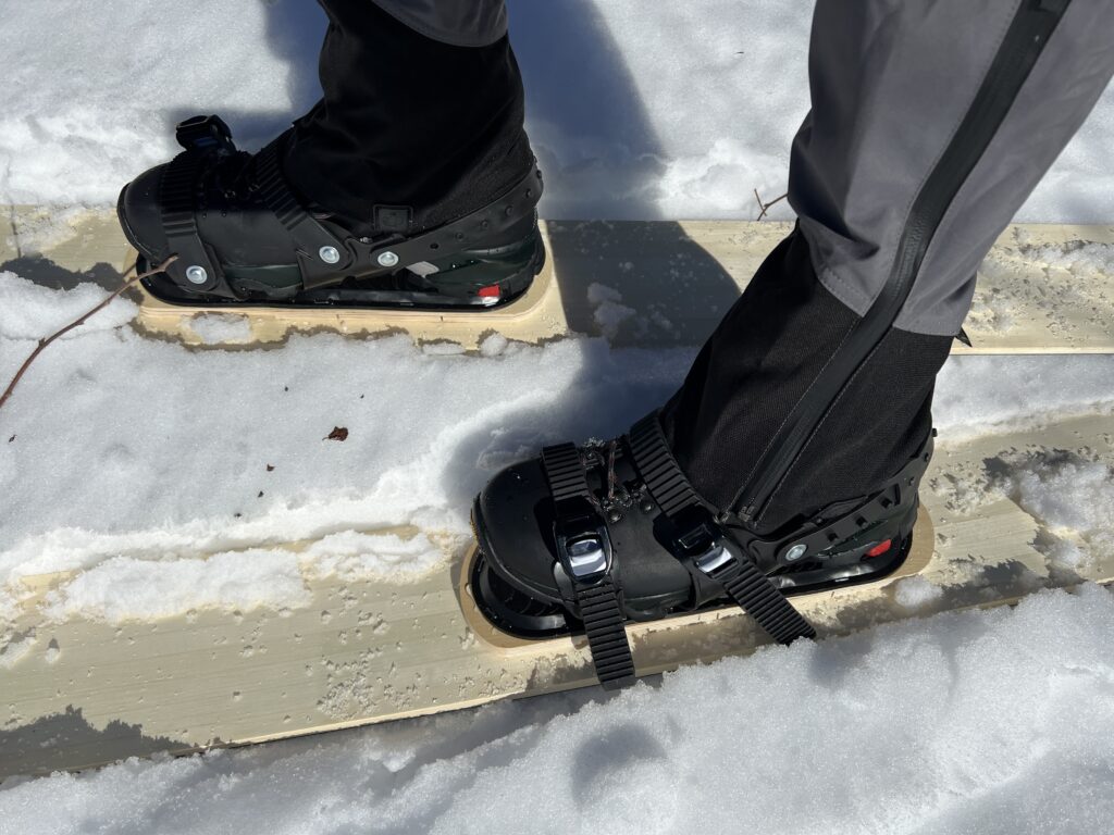 Pair of boots inside three strap bindings mounted on a skis placed on snow.