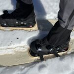 Pair of boots inside three strap bindings mounted on a skis placed on snow.