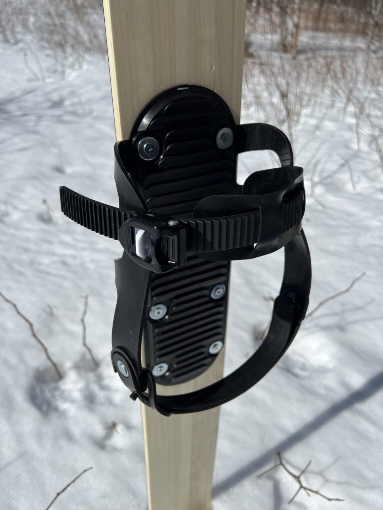 Two strap ski binding mounted on a ski placed in snow.